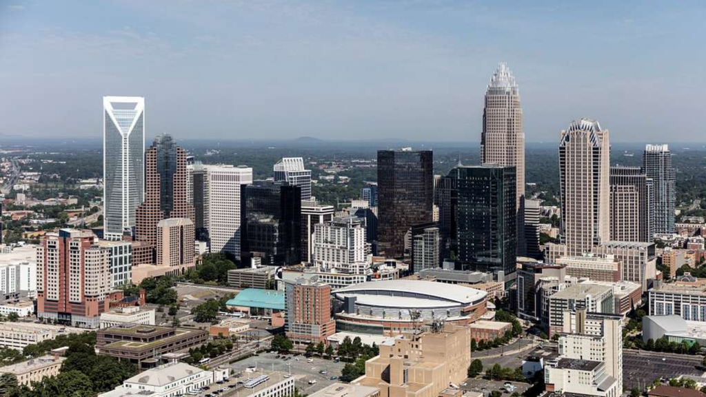 Aerial view of the downtown Charlotte, North Carolina skyline on a clear day, with the uptown high-rise cluster and arena in the foreground