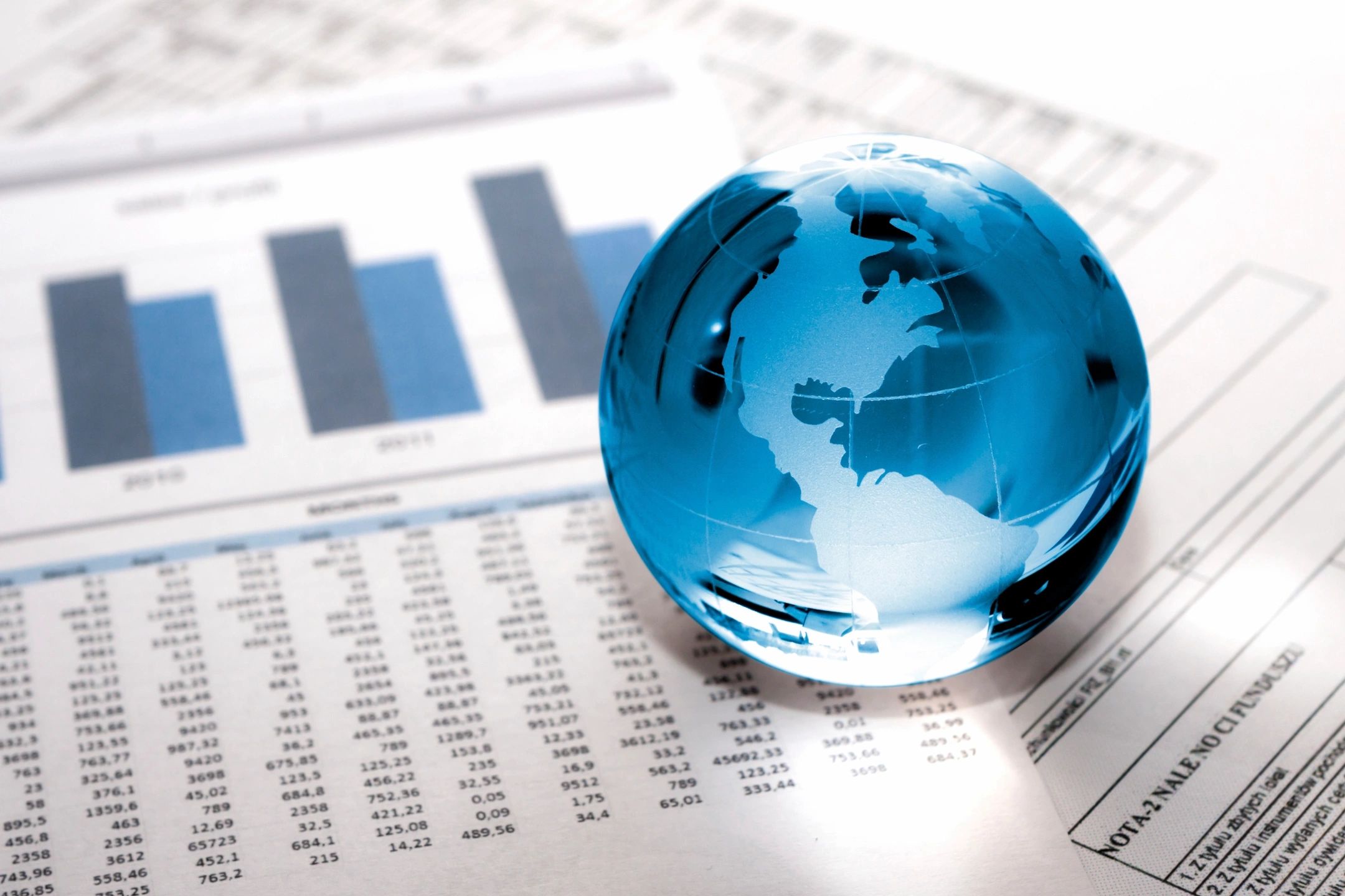 Glass globe resting on printed economic charts and data tables